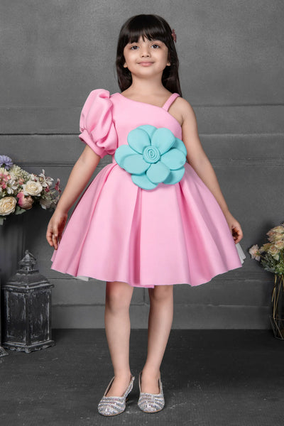 Young girl wearing a pink dress with a blue flower accessory against a gray background